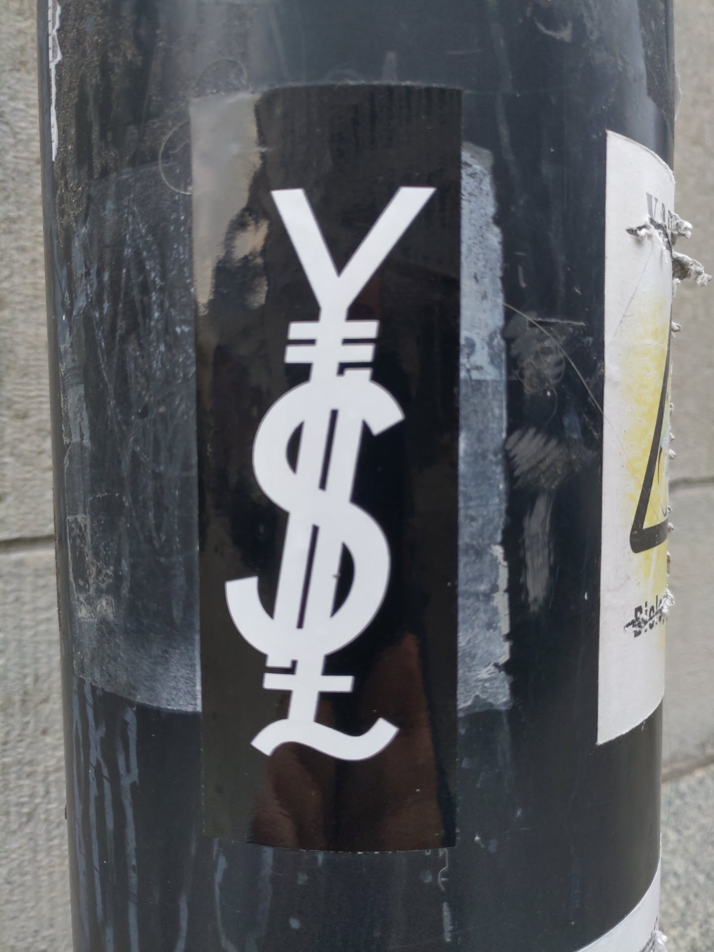 A black and white sticker featuring a stylized combination of the US dollar, Japanese yen, and British pound symbols. The design is minimalist and impactful.