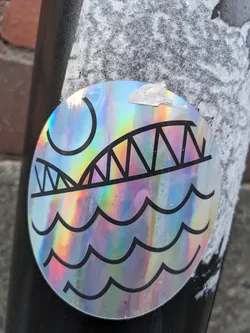 A round holographic sticker with a design depicting a bridge over wavy water, and a sun. The sticker has a rainbow effect due to the holographic material. The design is simple and minimalist, with black lines outlining the bridge, sun, and water.