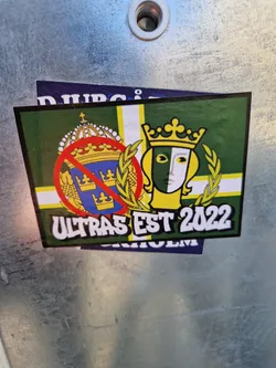 A sticker featuring a green and yellow flag with crowns and a masked face, along with the text 'Ultras Est 2022'.