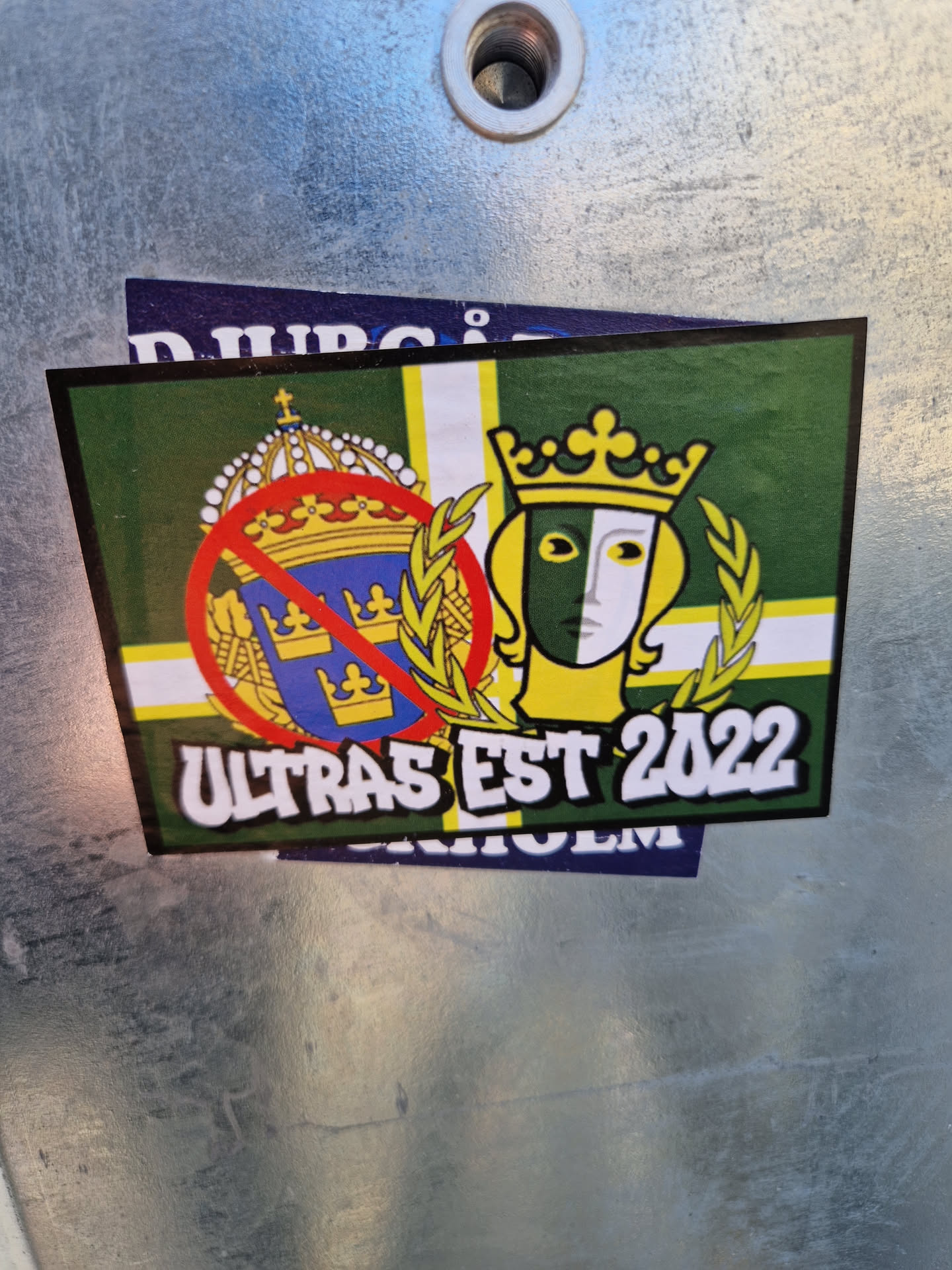 A sticker featuring a green and yellow flag with crowns and a masked face, along with the text 'Ultras Est 2022'.