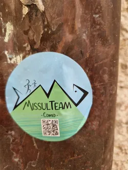 Round sticker with a logo featuring stylized mountains, two running figures, and the text "MissulTeam - Como."  A QR code is also present at the bottom.