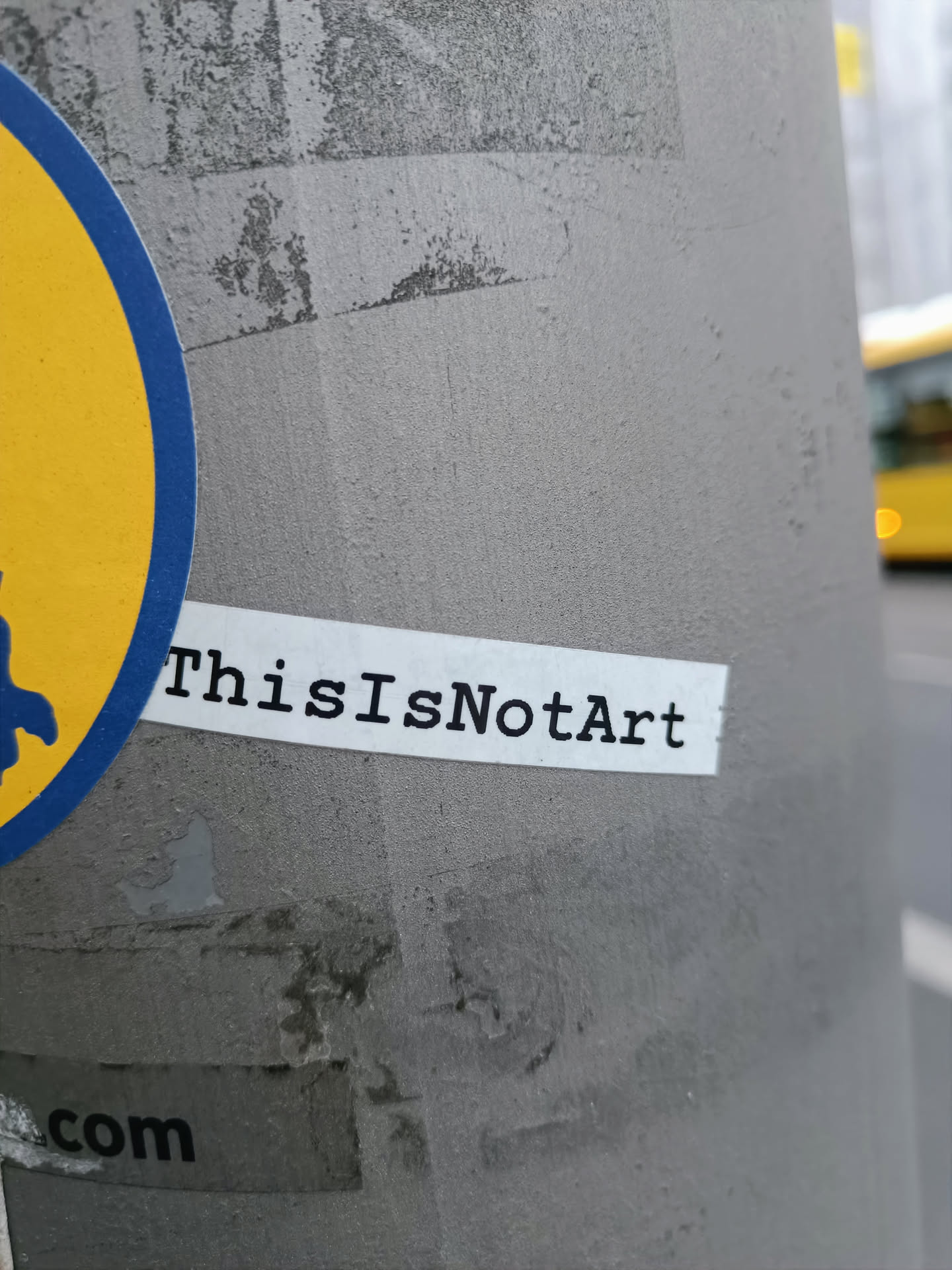 A minimalist sticker with the text "ThisIsN0tArt" printed on it. The sticker is affixed to a gray pole.