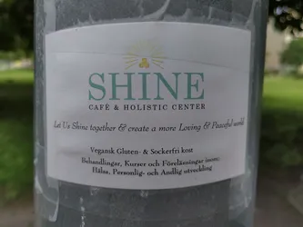Sticker for Shine Cafe & Holistic Center. The sticker promotes a vegan, gluten and sugar free menu and courses, treatments and lectures within health, personal and spiritual development.