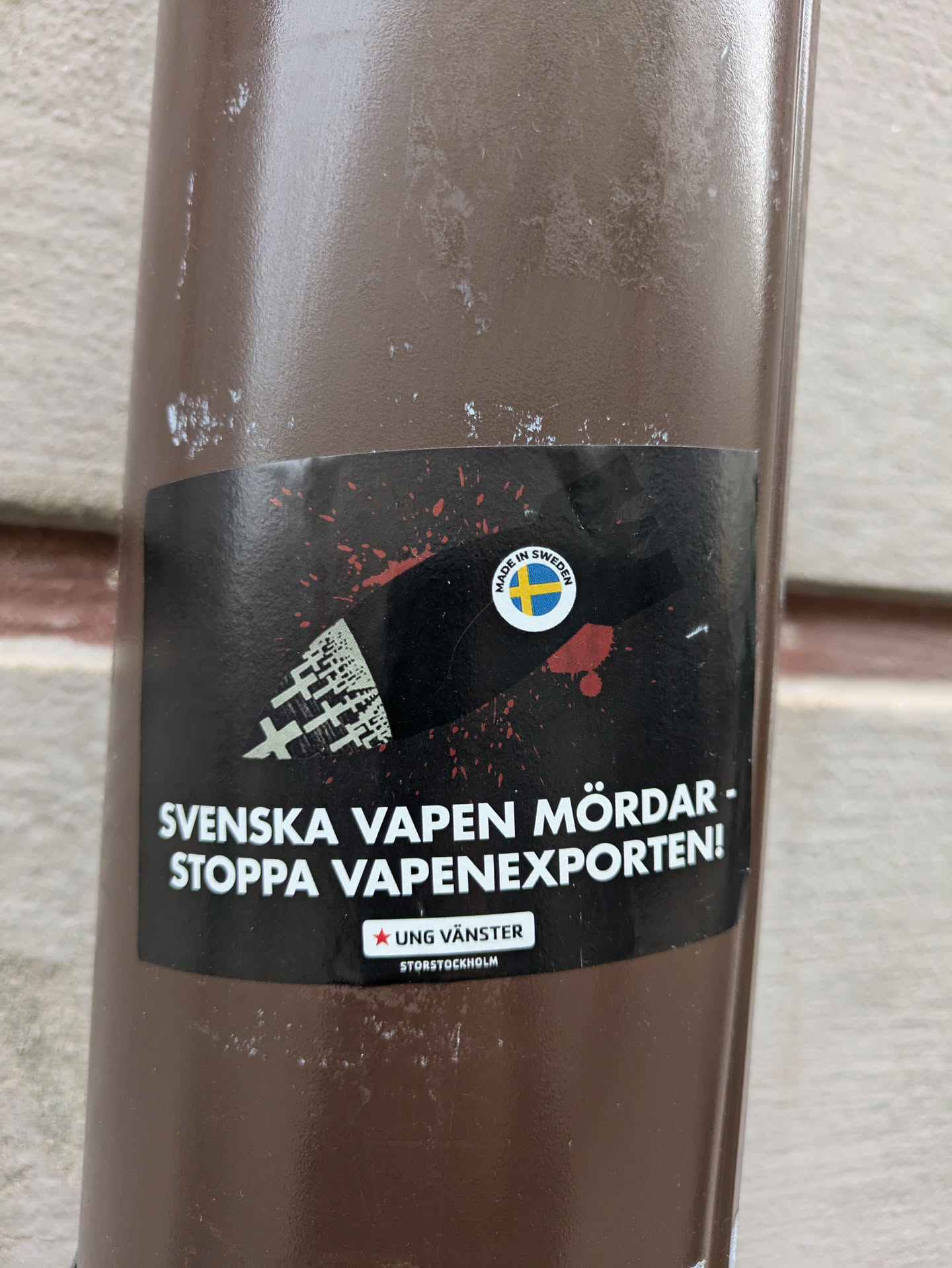 A sticker with a graphic depicting crosses and bloodstains, expressing opposition to Swedish arms exports.  The sticker has text in Swedish and a logo for Ung Vänster (Young Left) Stockholm.
