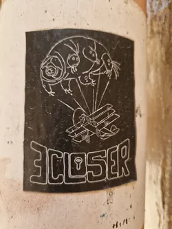 Black and white sticker featuring a stylized illustration of a tardigrade seemingly piloting a small biplane. The word 'CLOSER' is written in a stylized font at the bottom. The image is slightly worn, suggesting it's been affixed outdoors for some time.