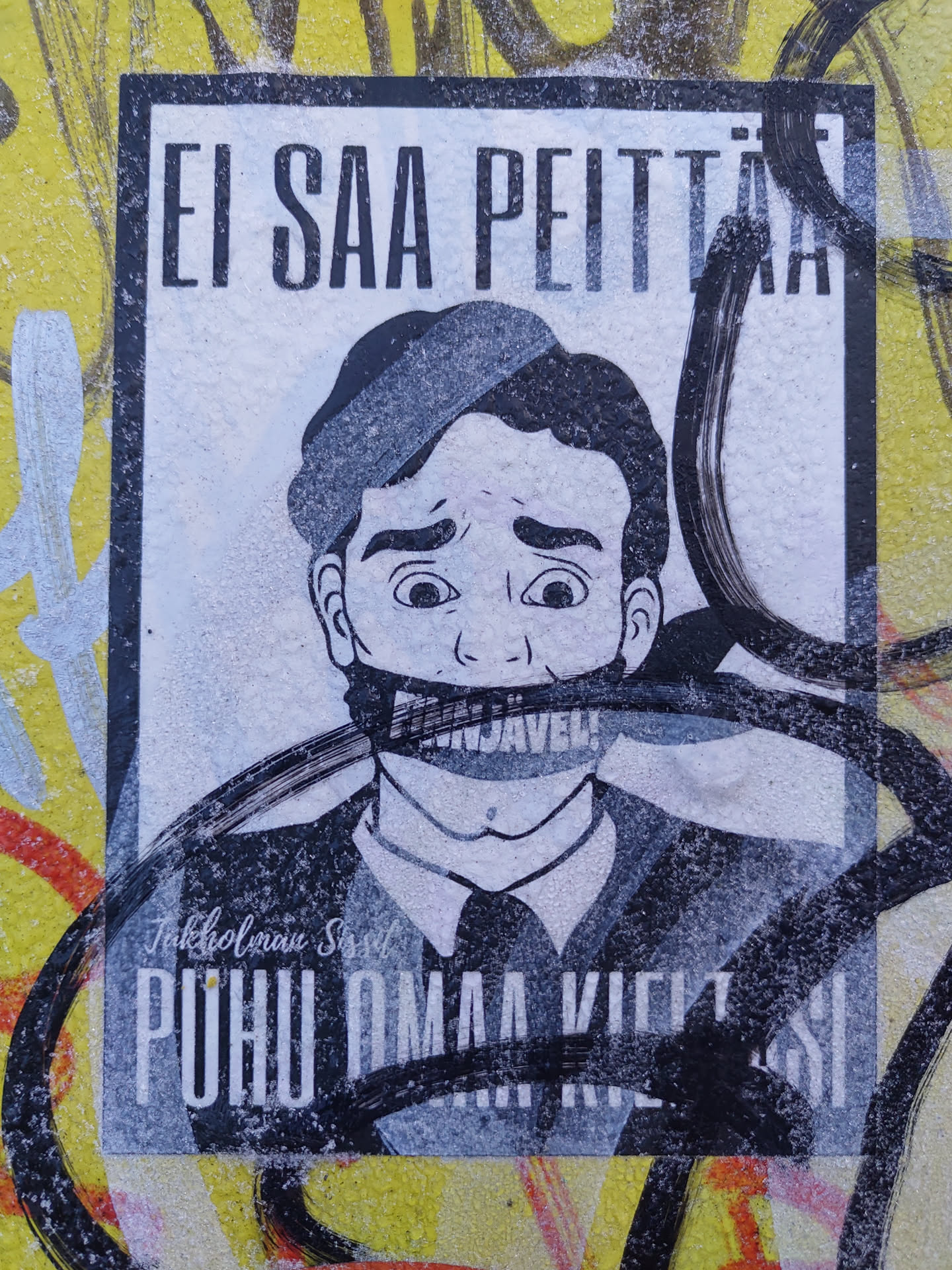 A sticker featuring a black and white illustration of a man with his mouth taped shut, with the text "Ei saa peittää" (Can't hide) at the top and "Puhu omaa kieltäsi" (Speak your own language) at the bottom. The sticker has a grunge and rebellious style. The man's mouth is covered with tape that says "Sensuuri".