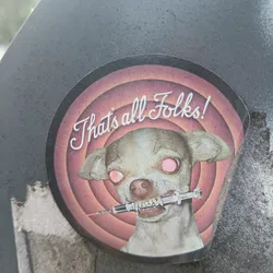 A round sticker featuring a chihuahua with glowing red eyes holding a syringe in its mouth.  The background is a retro-style target pattern with the text "That's all Folks!" in a stylized script font. The overall aesthetic is dark and humorous, referencing classic cartoon endings.