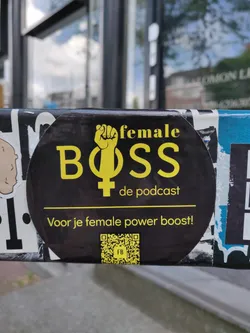A black and yellow sticker promoting a podcast called "Female Boss." It includes a raised fist and the female symbol. The text also says: "Voor je female power boost!" which translates to "For your female power boost!"