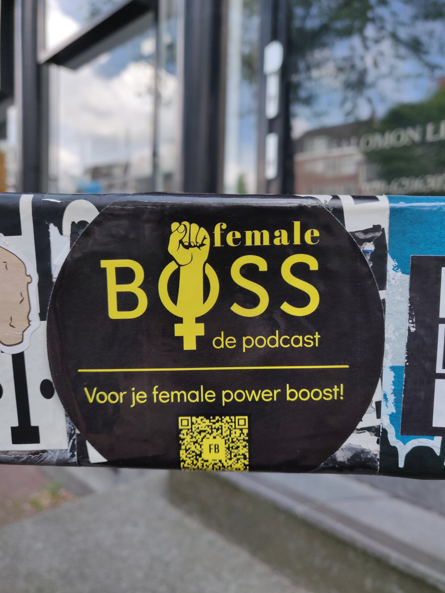 A black and yellow sticker promoting a podcast called "Female Boss." It includes a raised fist and the female symbol. The text also says: "Voor je female power boost!" which translates to "For your female power boost!"