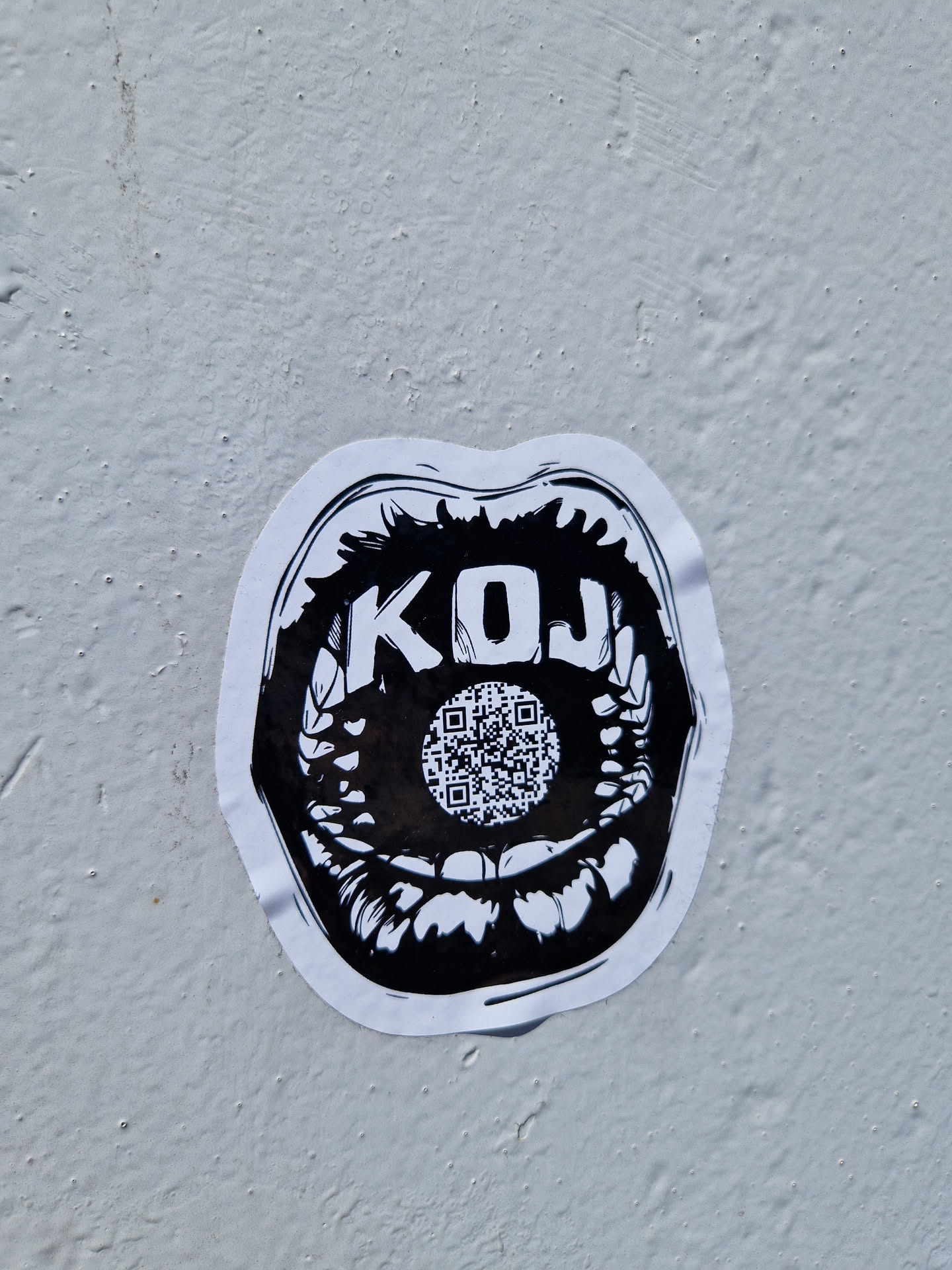 Black and white sticker depicting a mouth with the letters KOJ and a QR code in the center. The style is graphic and slightly edgy.