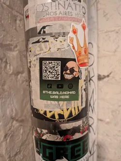 Street sticker A square promotional sticker with a dark background fading into forest green. On the upper half, it displays a square QR code next to a cartoon avatar of a smiling, bald man sporting a black beard and round dark sunglasses. Beneath them are three social media logos (TikTok, YouTube, and Instagram). At the bottom, stylized white text declares '@THE.BALD.NOMAD WAS HERE'.