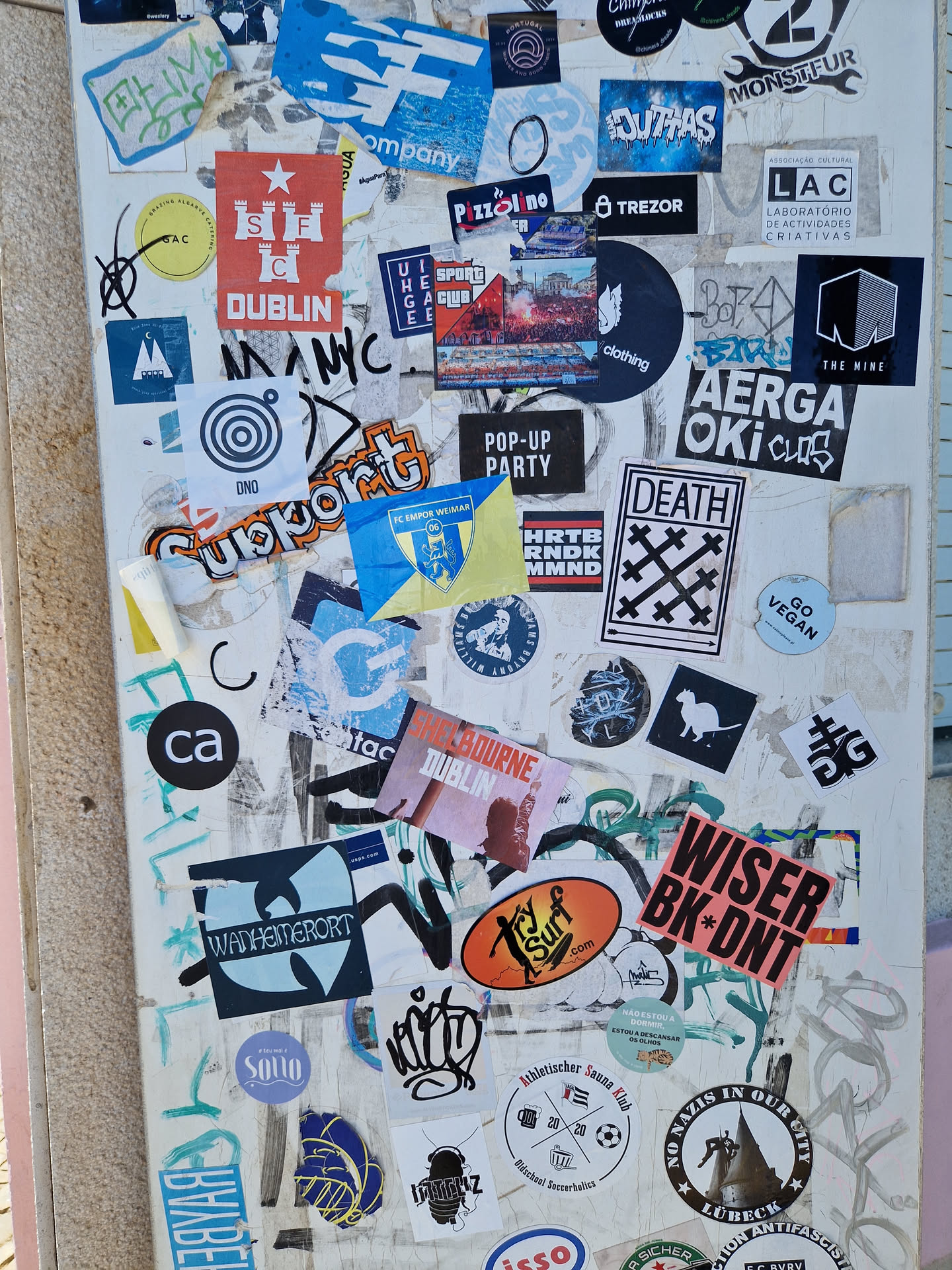A close-up shot of a sticker featuring a red star and a castle, with the word "DUBLIN" underneath. The sticker is part of a larger collection of stickers, graffiti, and tags on a white wall.  Many of the other stickers are illegible.