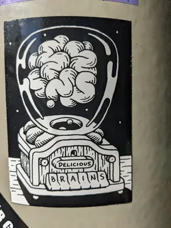 A black and white sticker depicting a brain inside a glass dome on top of a machine with the words "Delicious Brains" written on it.