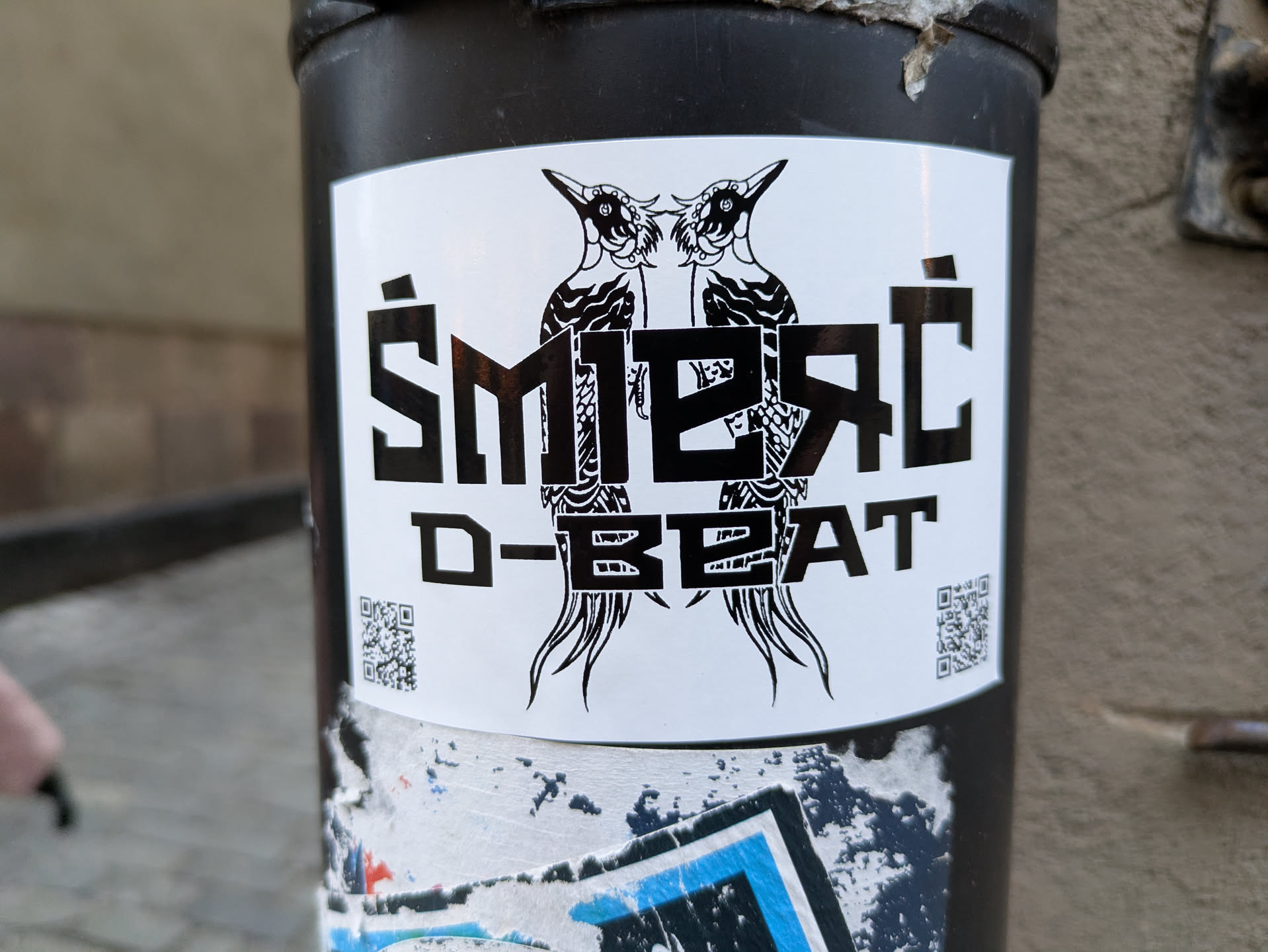 Black and white sticker with two birds and stylized text.  The text 'Smieřc D-BEAT' is prominent.  There are QR codes on either side of the central design.