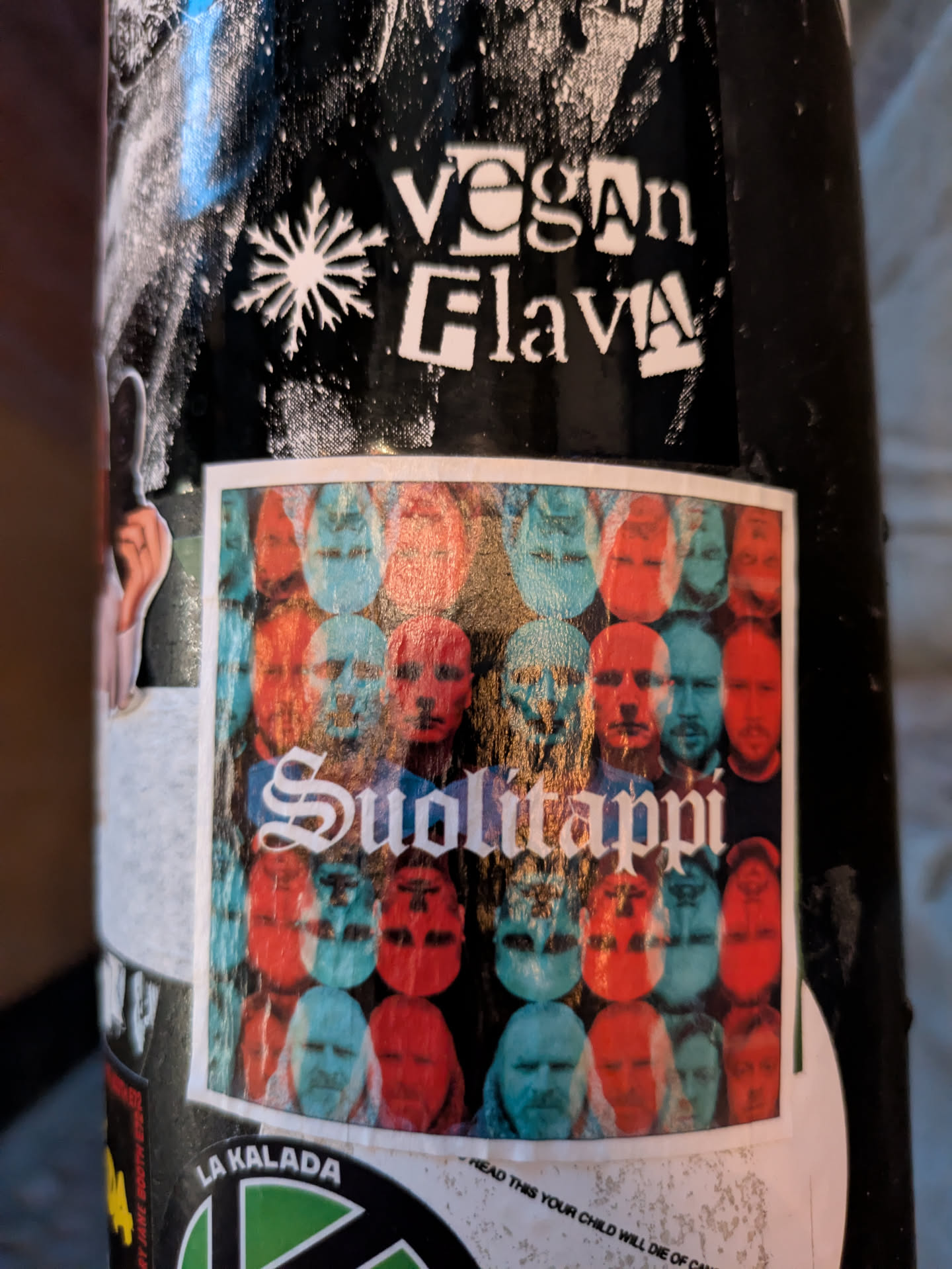 The central sticker is a rectangular, slightly distressed piece featuring a collage of human faces. The faces are rendered in a limited color palette of red and cyan, creating a ghostly, layered effect. They are arranged in a grid-like pattern, with some faces appearing upright and others inverted. The word 'Suolitappi' is prominently displayed in the center in a stylized, gothic-style font with white lettering and a subtle shadow. The overall impression is abstract and slightly unsettling, with a vintage or experimental artistic feel.