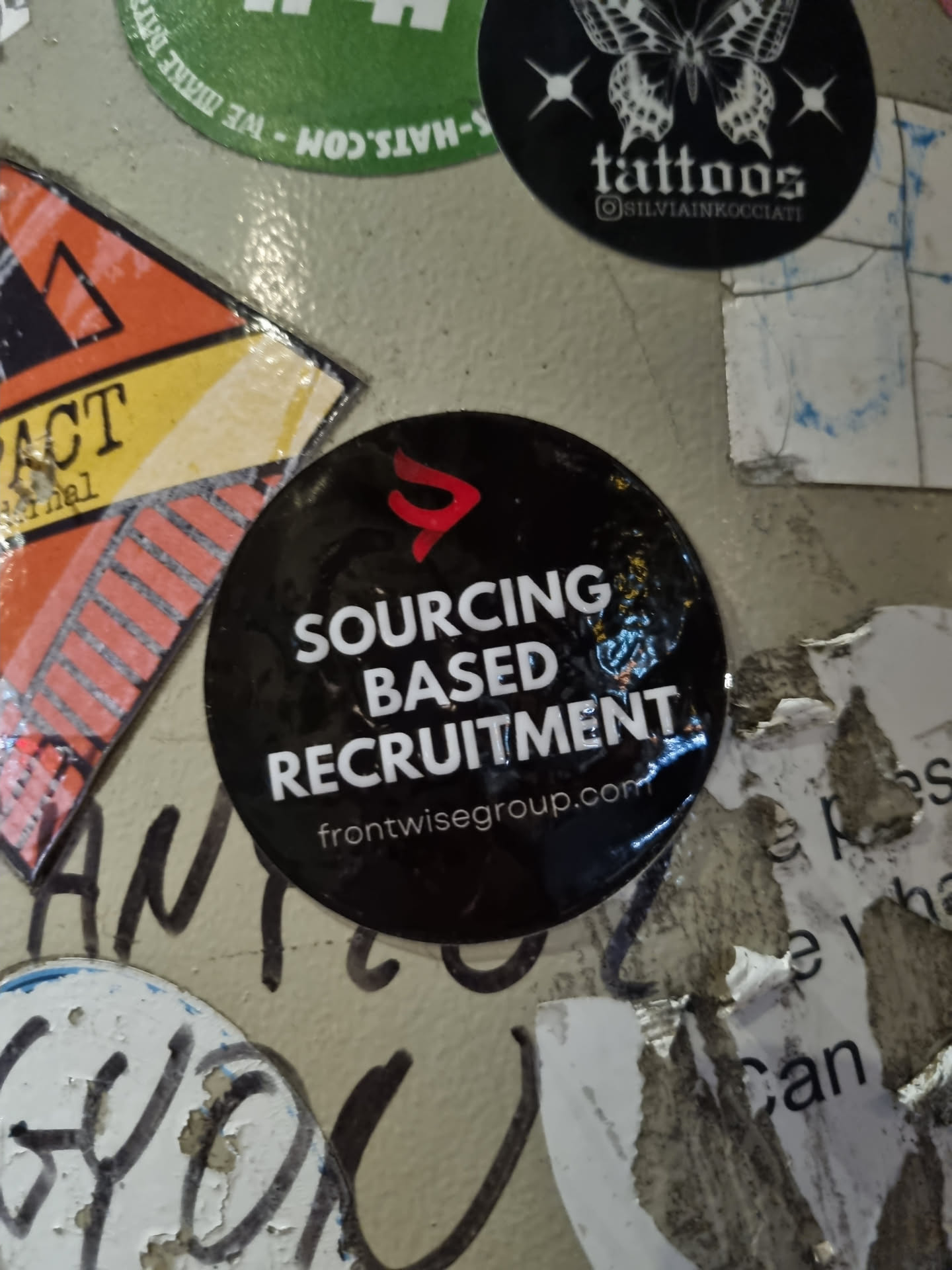 A black round sticker with the text "SOURCING BASED RECRUITMENT" and the website frontwisegroup.com. The sticker has a red logo in the upper left corner.