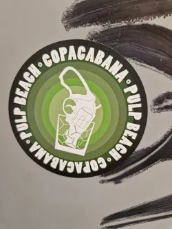 Round sticker with a green and white design. It features a drawing of a cocktail shaker pouring a drink into a glass, encircled by the text "Pulp Beach Copacabana" repeated twice in a circular fashion.