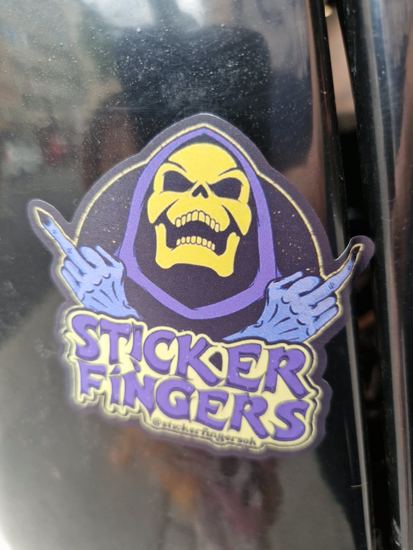 A sticker featuring Skeletor from He-Man, giving the middle finger with both hands. The text "Sticker Fingers" is written below the illustration, with a small social media handle visible at the bottom.