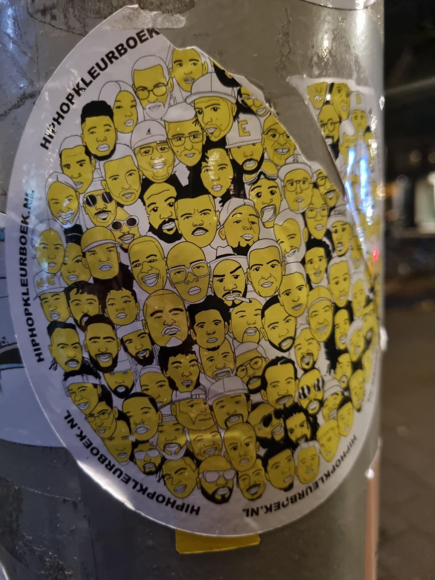 Round sticker with many yellow and black illustrated portraits of hip-hop artists. The text 'HipHopKleurboek.nl' is visible around the edge.