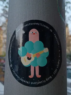 Round sticker featuring an illustration of a pink humanoid figure with teal puffy sleeves playing an acoustic guitar. The background is black with white speckles. The text around the character says "www.jenseitsvonmillionen.de - Festival - 5 + 6 August 2022 - Burgfriedland (Niedersachsen)" and "@jenseitsvonmillionen".