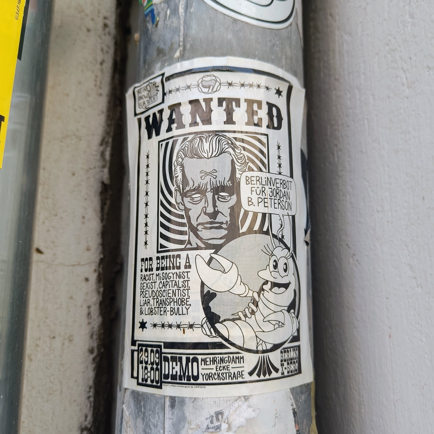 A black and white sticker in the style of a wanted poster. It depicts a caricature of Jordan B. Peterson with a lobster beside it, accusing Peterson of various negative traits and announcing a Berlin demonstration.