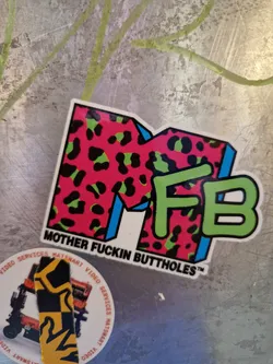 A sticker with a stylized "MF" logo in a pink and green leopard print. The text "Mother Fuckin Buttholes" is written below the logo.