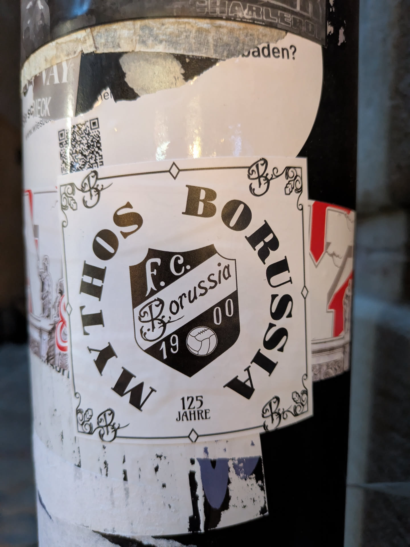 The sticker is square-shaped with a white background and a black border. It features ornate black decorative elements in the corners. In the center is a shield-shaped crest with the text 'F.C. Borussia' and '19 00' within it, along with a stylized football. The words 'MYTHOS' and 'BORUSSIA' are printed in large, bold, black capital letters curving around the crest. Below the crest, the text '125 JAHRE' is visible.