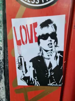 Black and white sticker featuring a stylized woman holding a spray can with the word LOVE painted in red dripping down the can.