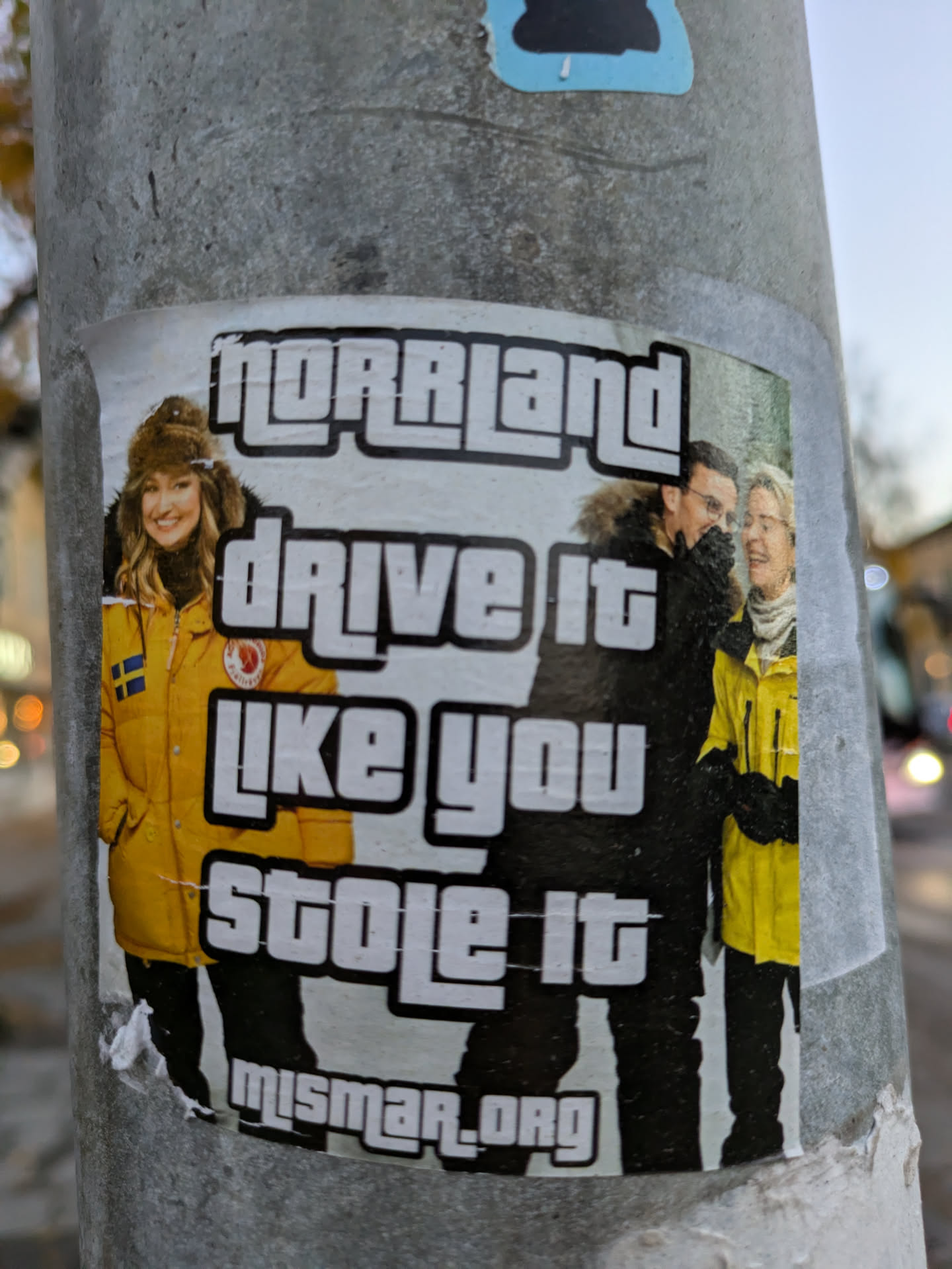 Sticker featuring three people wearing yellow winter jackets with the text "Norrland" and "Drive it like you stole it" in a style reminiscent of the Grand Theft Auto video game series.  The bottom features a website address.