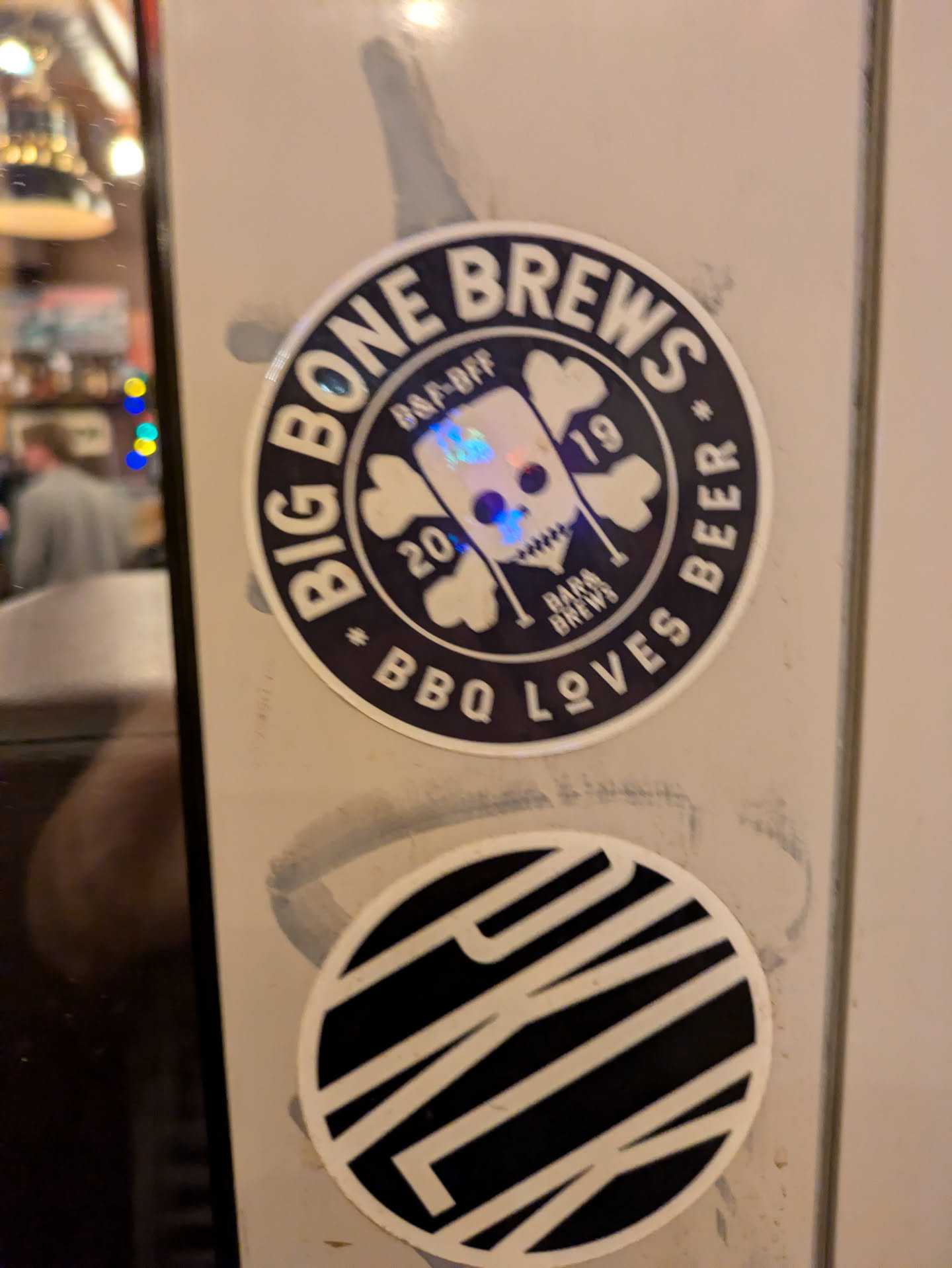 A round sticker featuring the logo of Big Bone Brews, a brewery.  The logo includes a skull design with crossed bones, text that says "Big Bone Brews" and "BBQ Loves Beer." There is also some smaller text indicating a "2019 BBQ-Off".