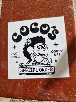 A sticker featuring a cartoon illustration of a girl behind a DJ mixer with the text "Coco's" at the top, "Special Order" at the bottom and "Hot one... Comin' up!" on either side. The style is reminiscent of 70s-80s cartoons.