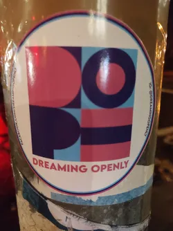 Round sticker featuring a geometric design in pink, blue, and dark purple. The text 'DREAMING OPENLY' is printed at the bottom.  Social media links are present for Instagram and Facebook.