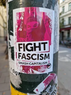 A sticker featuring a person wearing a balaclava with the text 'FIGHT FASCISM' and 'SMASH CAPITALISM'.