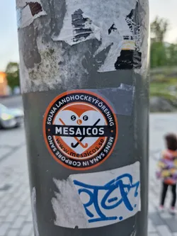 Round orange and white sticker with the text "Solna Landhockeyförening" and the logo of Mesaicos.  The website www.mesaicos.se is also on the sticker.