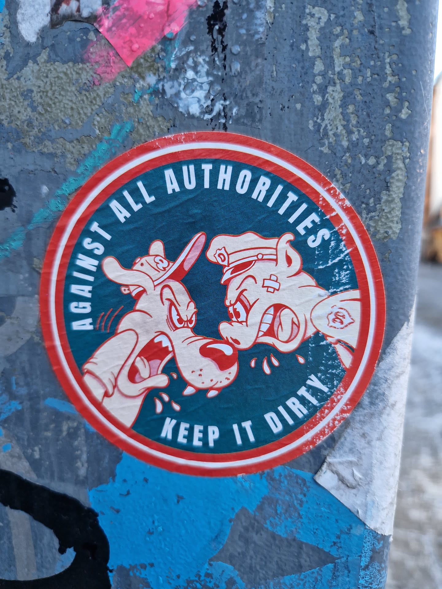 Round sticker featuring two cartoon dogs facing off. One dog wears a cowboy hat, the other a police hat. The text on the sticker says "Against All Authorities" at the top and "Keep it Dirty" at the bottom.