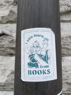 A sticker featuring a cartoon character reading a book. The text on the sticker says "I also learn from BOOKS".