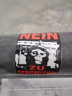 A black and white sticker with a chimpanzee in a cage and the text "NEIN ZU TIERVERSUCHEN" which translates to "No to animal testing".