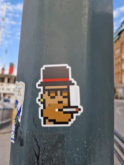 A pixel art sticker depicting a potato character wearing a hat and holding a cigarette. The sticker has a retro 8-bit video game aesthetic. 