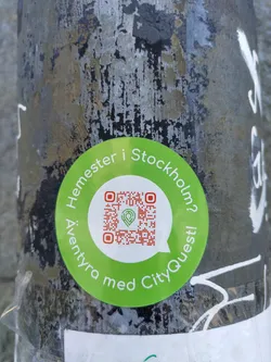 A round green sticker with a QR code in the center. The text around the QR code says "Äventyra med CityQuest!" and "Hemester i Stockholm?"