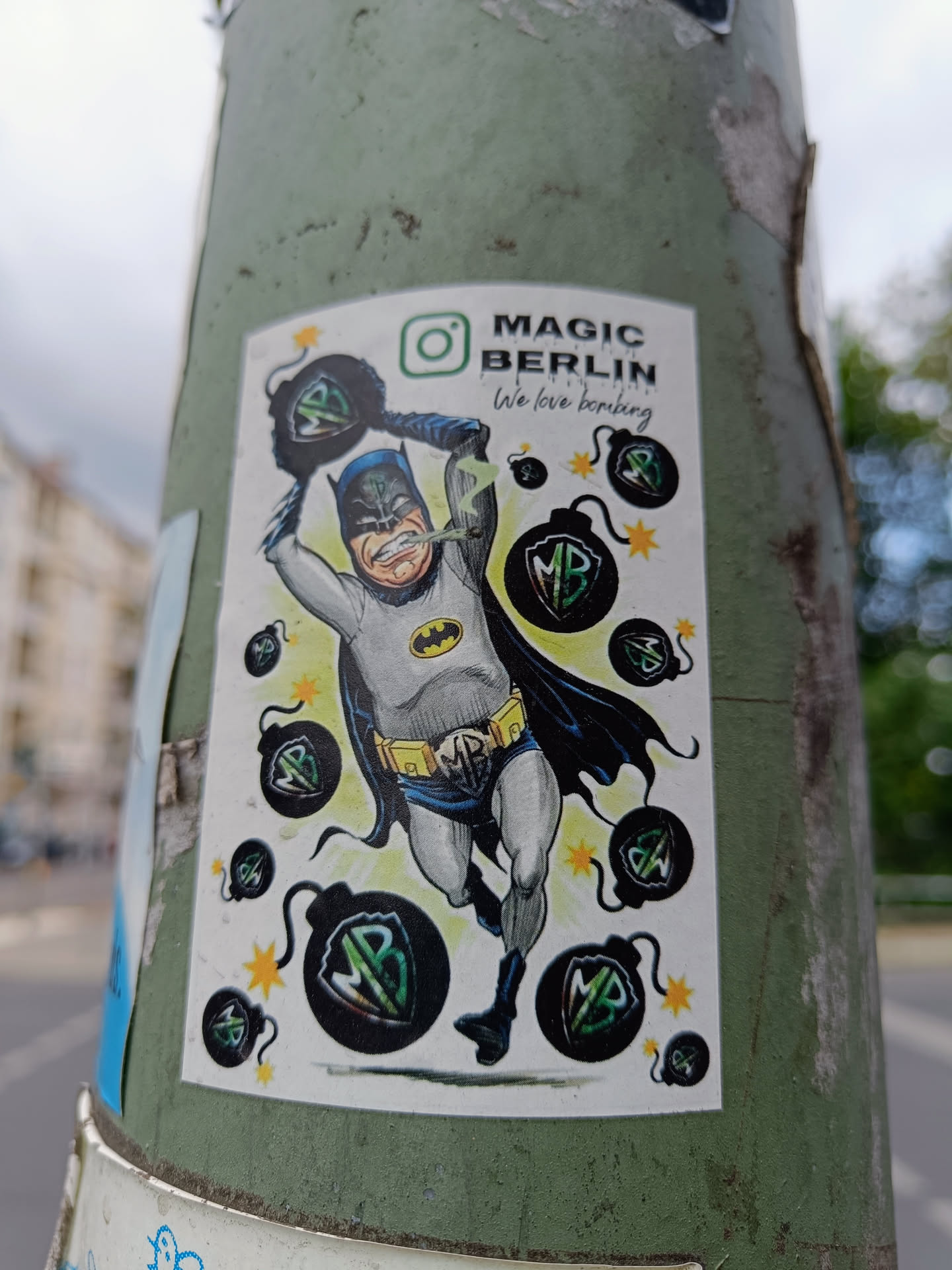 A sticker featuring a stylized illustration of Batman defusing bombs.  The design includes the text "MAGIC BERLIN" and "We love bombing", suggesting a playful, artistic commentary. Several bombs feature a stylized "MB" logo. An Instagram icon is also present. 