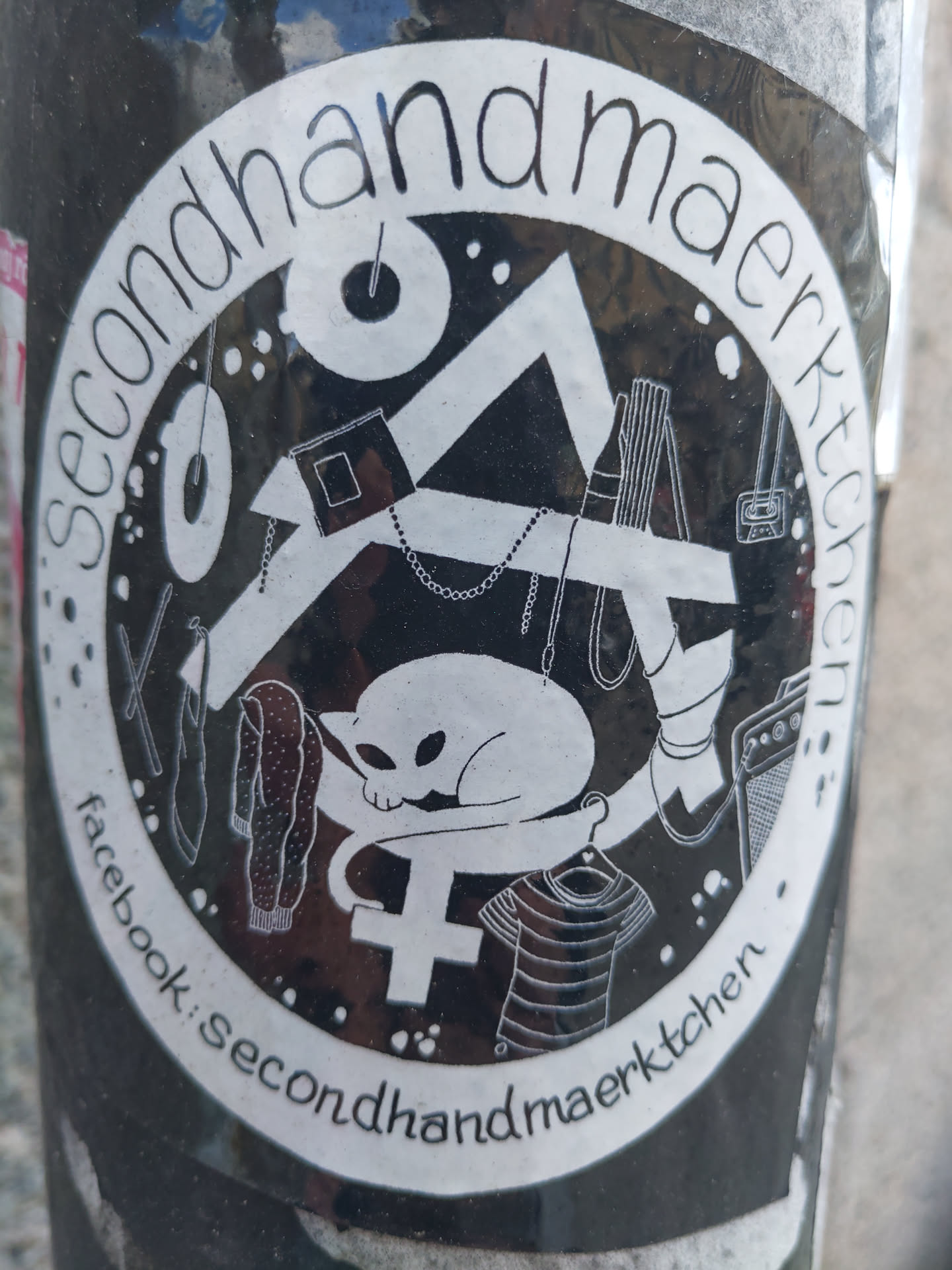 Black and white circular sticker with illustrations of various secondhand items and a cat resting on a plus symbol.  The text 'Secondhand Marktchen' is written around the circle, and 'facebook: secondhandmarktchen' is written at the bottom. 