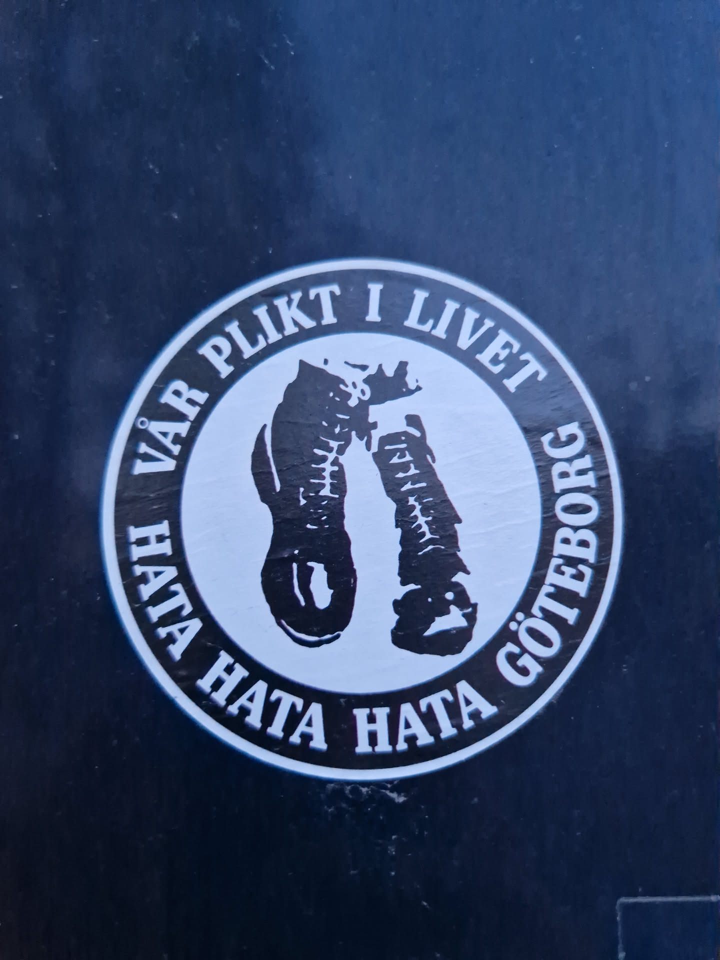 This sticker is black and white and circular. It shows two boots with text around them. The text is in Swedish and translates to "Our duty in life hate hate hate Gothenburg". The design is simple but striking. It's likely a statement piece expressing a strong opinion.