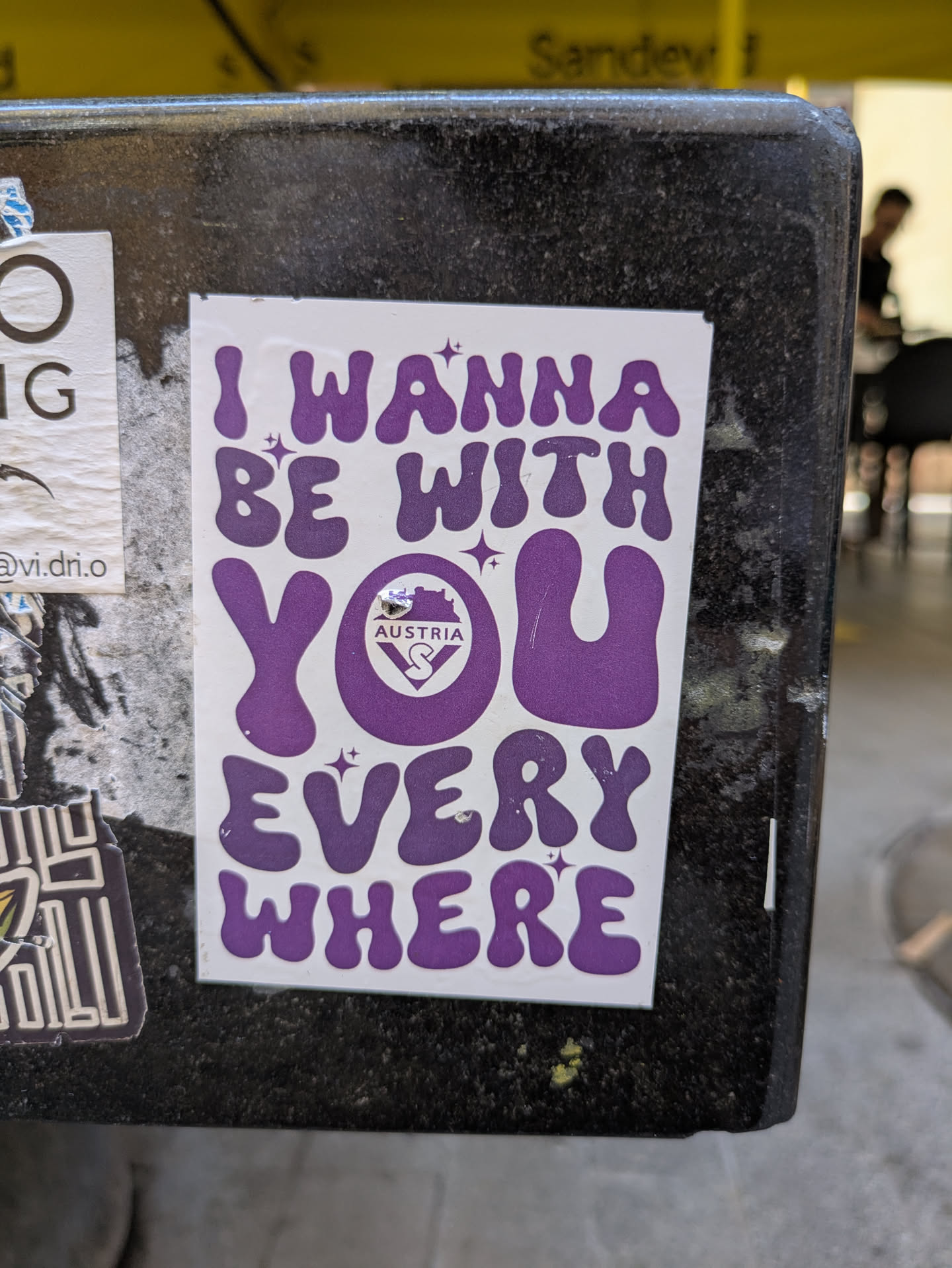 A sticker with the text "I wanna be with you everywhere". The text is purple and stylized with a retro vibe. The 'O' in 'You' contains the flag of Austria.