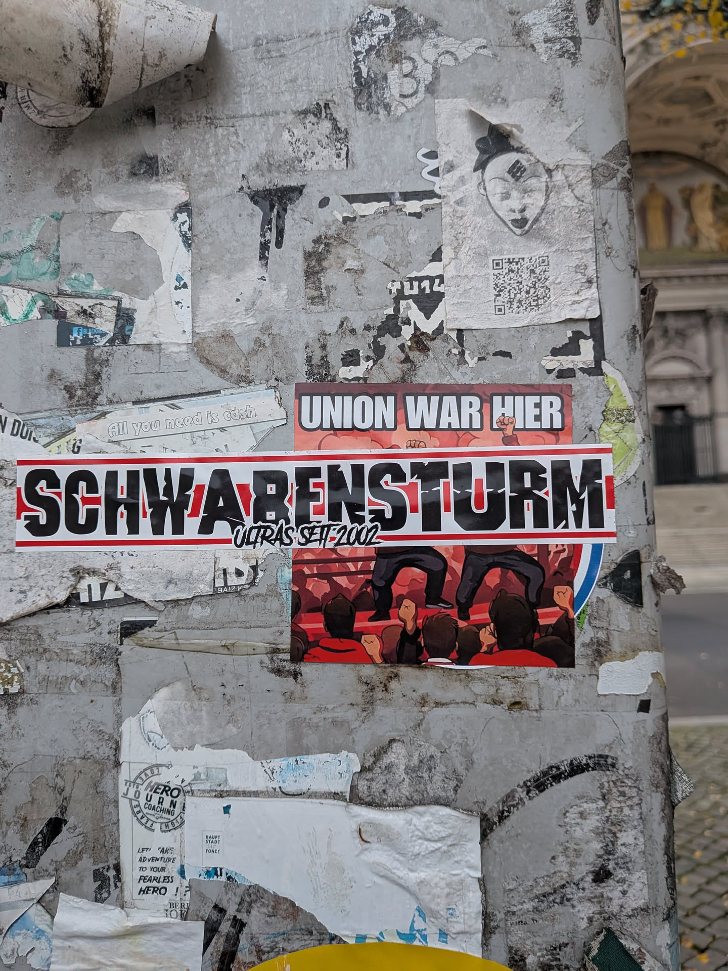 A horizontal rectangular sticker featuring large, bold, black block letters reading 'SCHWABENSTURM' with a white contour, set against horizontal red stripes on a white background. Underneath the center letters, the secondary text 'ULTRAS SEIT 2002' is rendered in a black handwritten/graffiti font outlined in white. The sticker is pasted directly over another football sticker showing fans and the text 'UNION WAR HIER'.