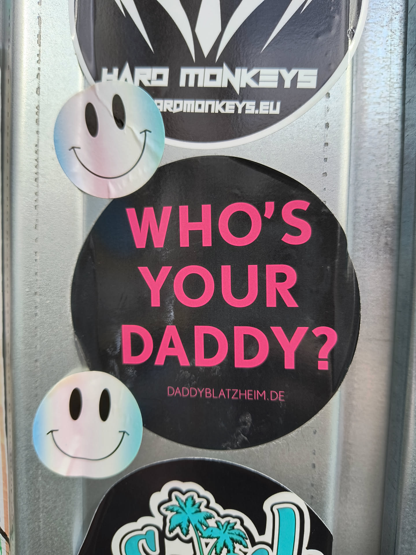 A black round sticker with the text "Who's your Daddy?" in hot pink.  There is a small website address at the bottom: daddyblatzheim.de