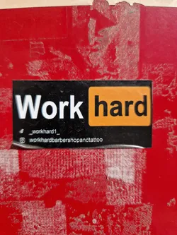 Black and orange sticker with the text "Work hard" and social media handles.
