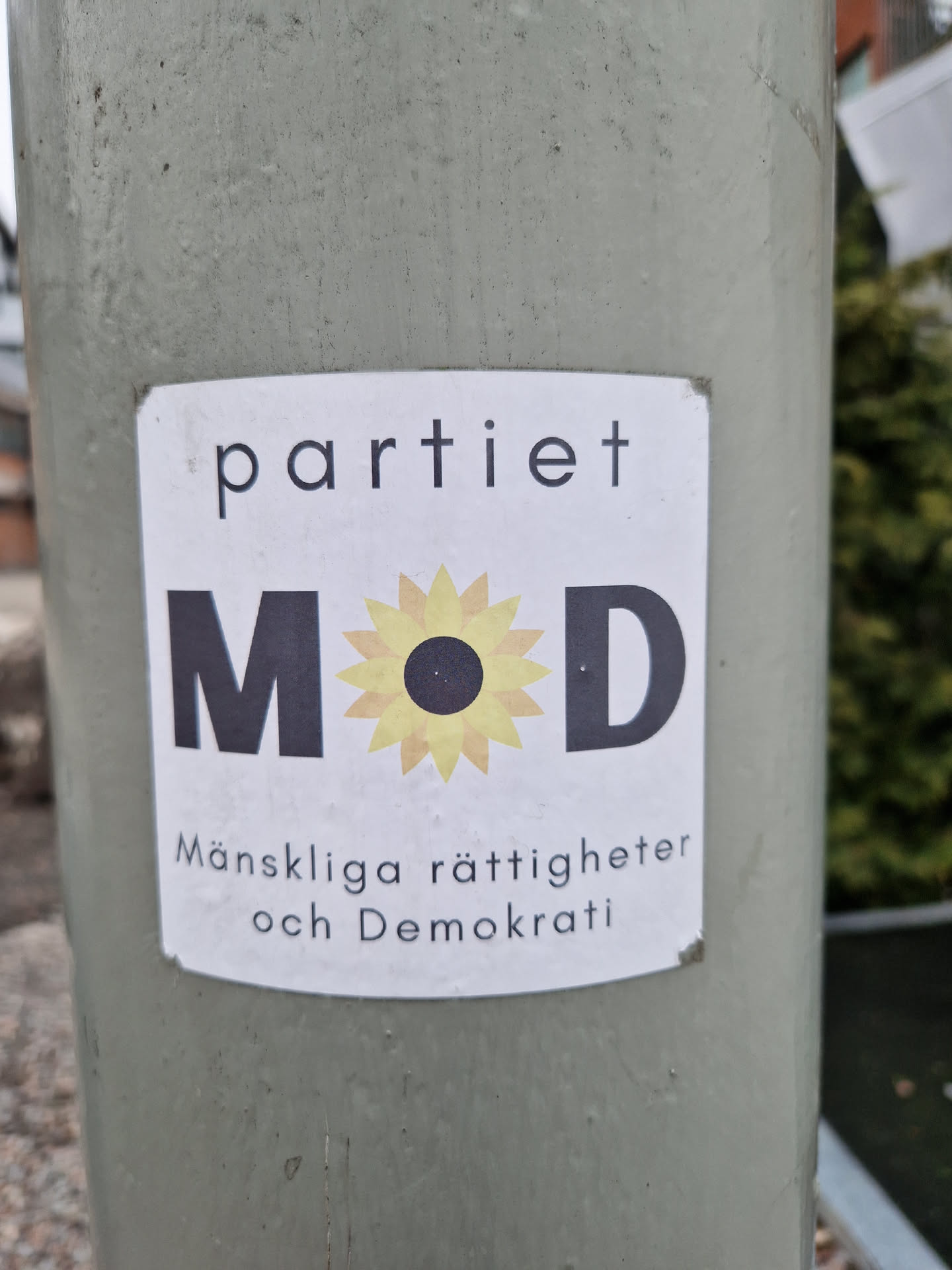 Sticker for the political party Månskliga rättigheter och Demokrati (Human Rights and Democracy) in Sweden.  The sticker features the party's logo, which includes the letters "MOD" and a stylized sunflower.