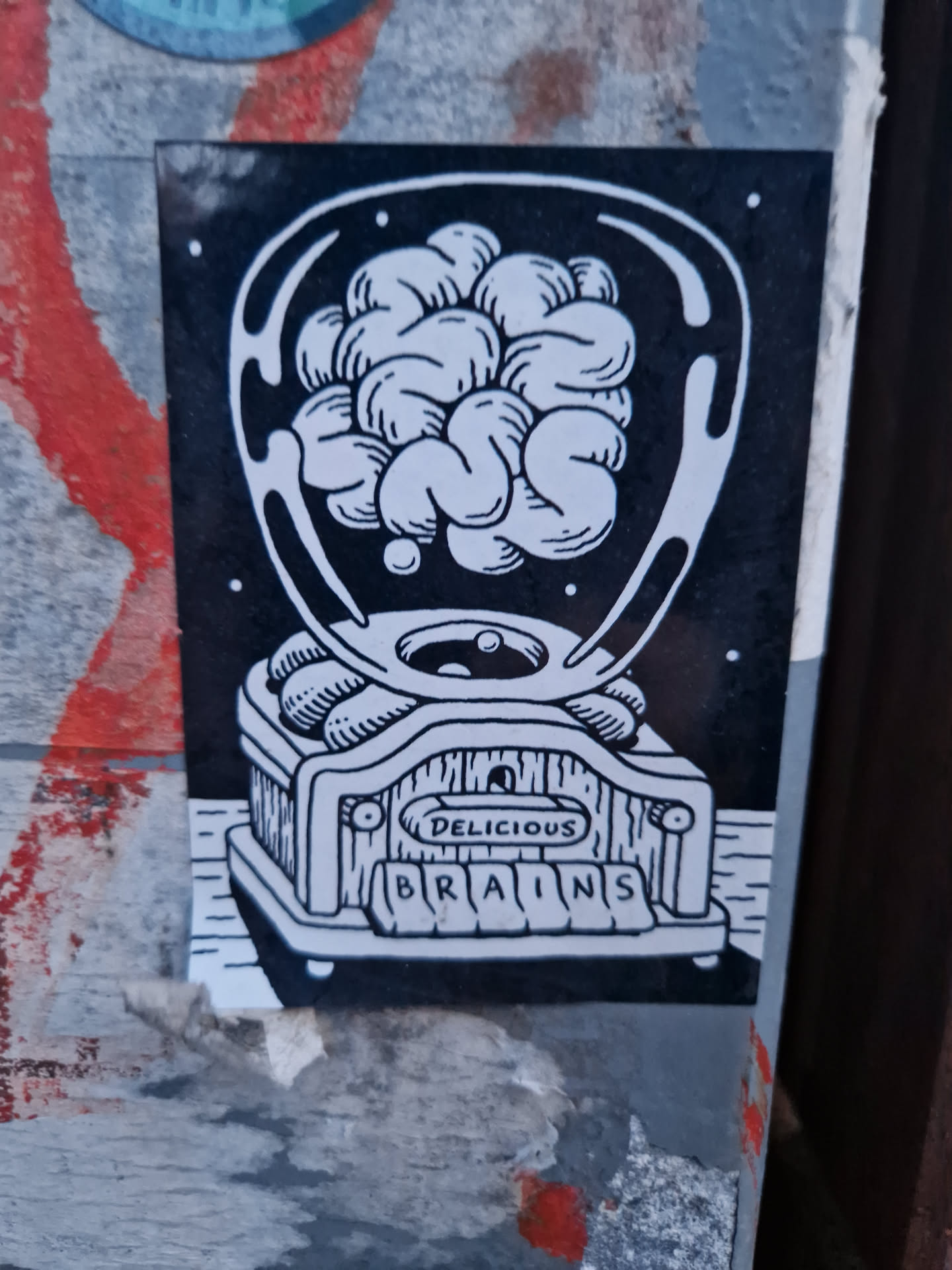 A sticker featuring a brain inside a device with the words 'Delicious Brains' on it. The style is black and white with a cartoonish illustration.