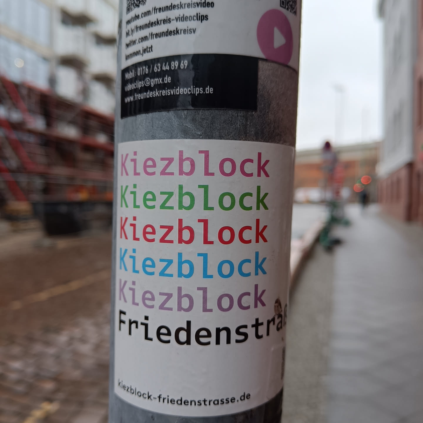 A sticker with the text "Kiezblock" repeated five times in different colors and "Friedenstraße" at the bottom.  A website address is also visible at the bottom. 