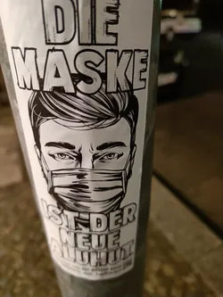 Black and white sticker featuring an illustration of a man wearing a face mask. The text on the sticker says "Die Maske ist der neue Hut" which translates from German to English as "The mask is the new hat".